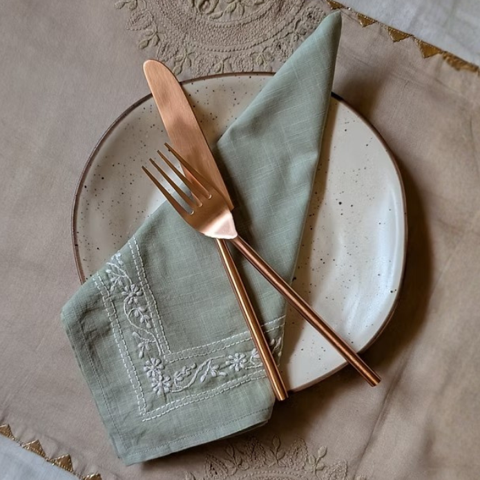 Set table with a plate, Chikankari sage green napkin, and cutlery on an Chikankari hand embroidered table runner and tablecloth.