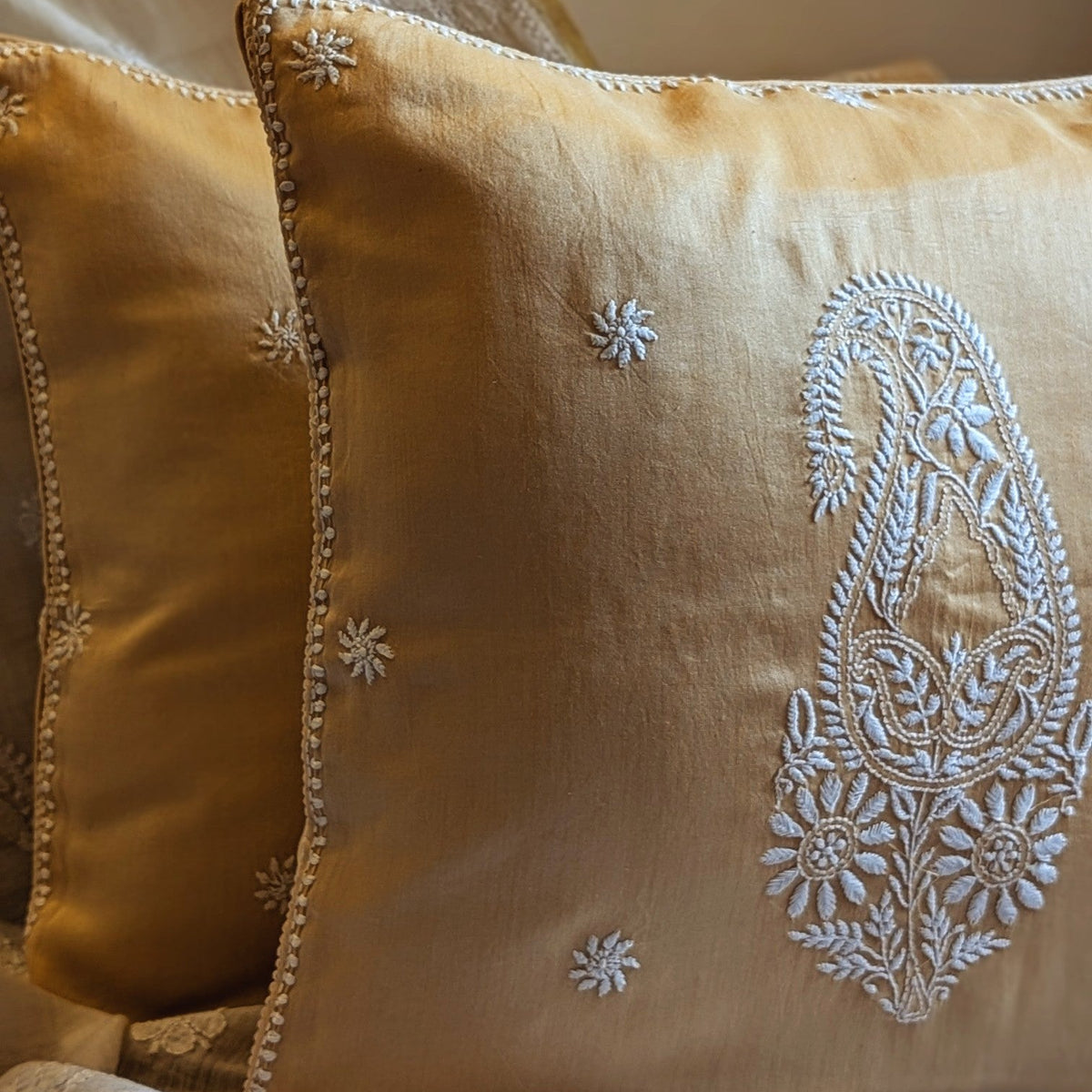 Gold pillow with intricate white embroidery on a silk textured surface