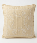A square beige Chikankari throw pillow with white floral embroidery in the center and a braided rope trim along the edges, shown against a plain white background.