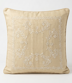 A square beige Chikankari throw pillow with white floral embroidery in the center and a braided rope trim along the edges, shown against a plain white background.