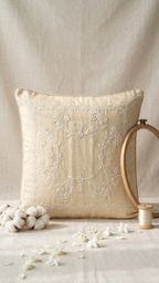 A square beige Chikankari cushion cover pillow with white floral embroidery in the center and a braided rope trim along the edges, shown a neutral backdrop