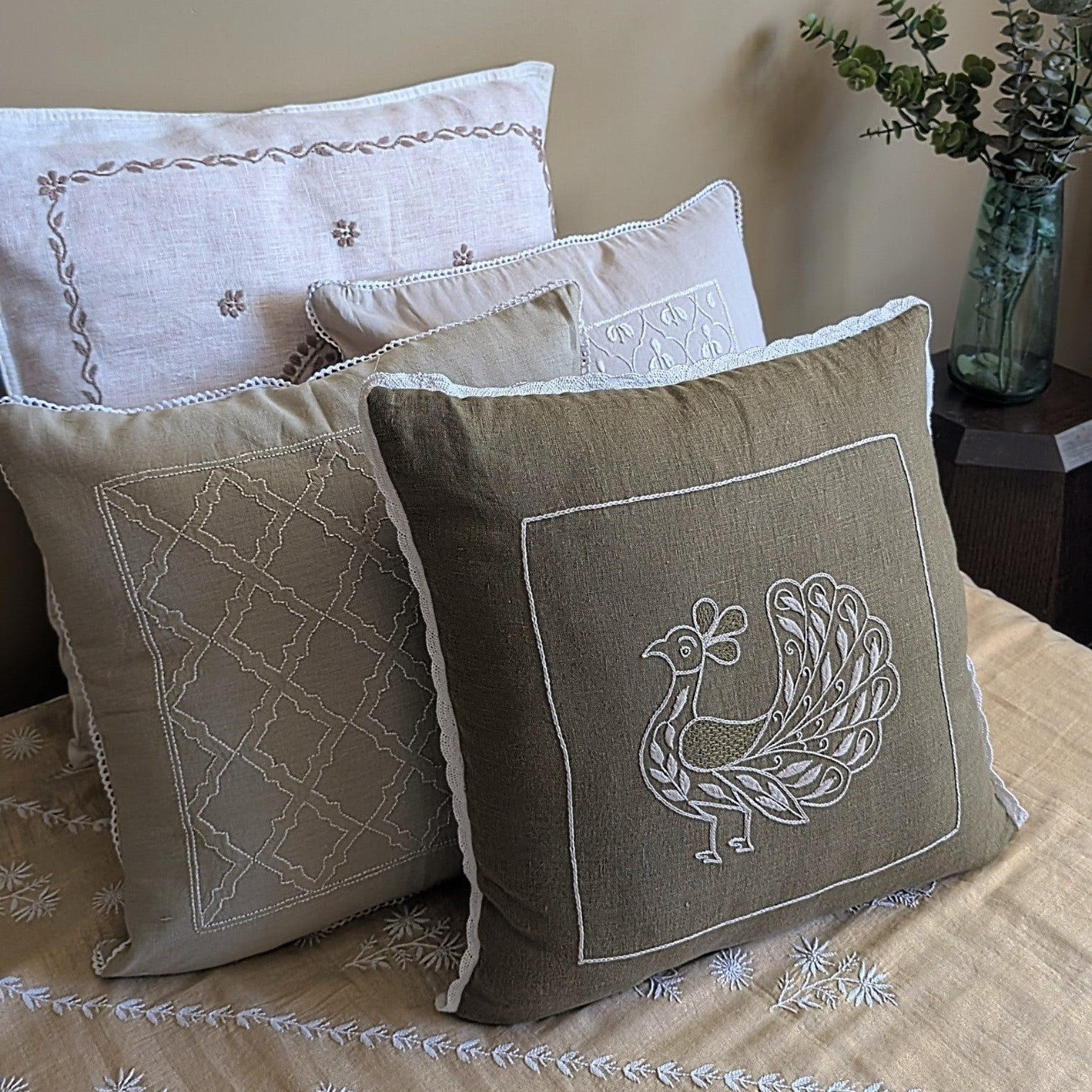 Decorative pillows with embroidered designs on a bed with a neutral background