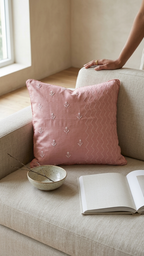 Chikankari pinkthrow pillow featuring a white embroidered paisley motif in the center and small white embroidered flowers scattered around it, set on a sofa