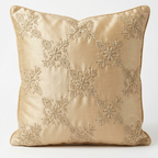A square decorative throw pillow in a champagne beige satin fabric, featuring an embroidered pattern of snowflakes and floral motifs.