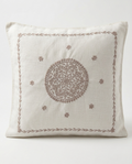 A square off-white linen throw pillow featuring a brown embroidered central mandala and a matching decorative border, set against a plain light gray background.