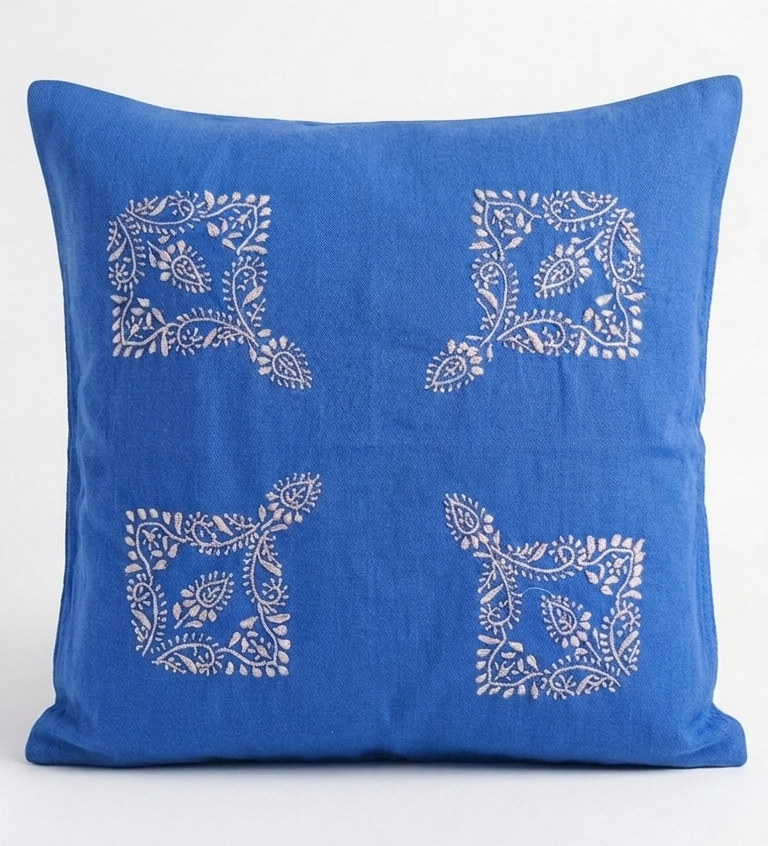 A square blue throw pillow with brown chikankari embroidered floral motifs arranged in a four-quadrant pattern, shown against a plain white background.